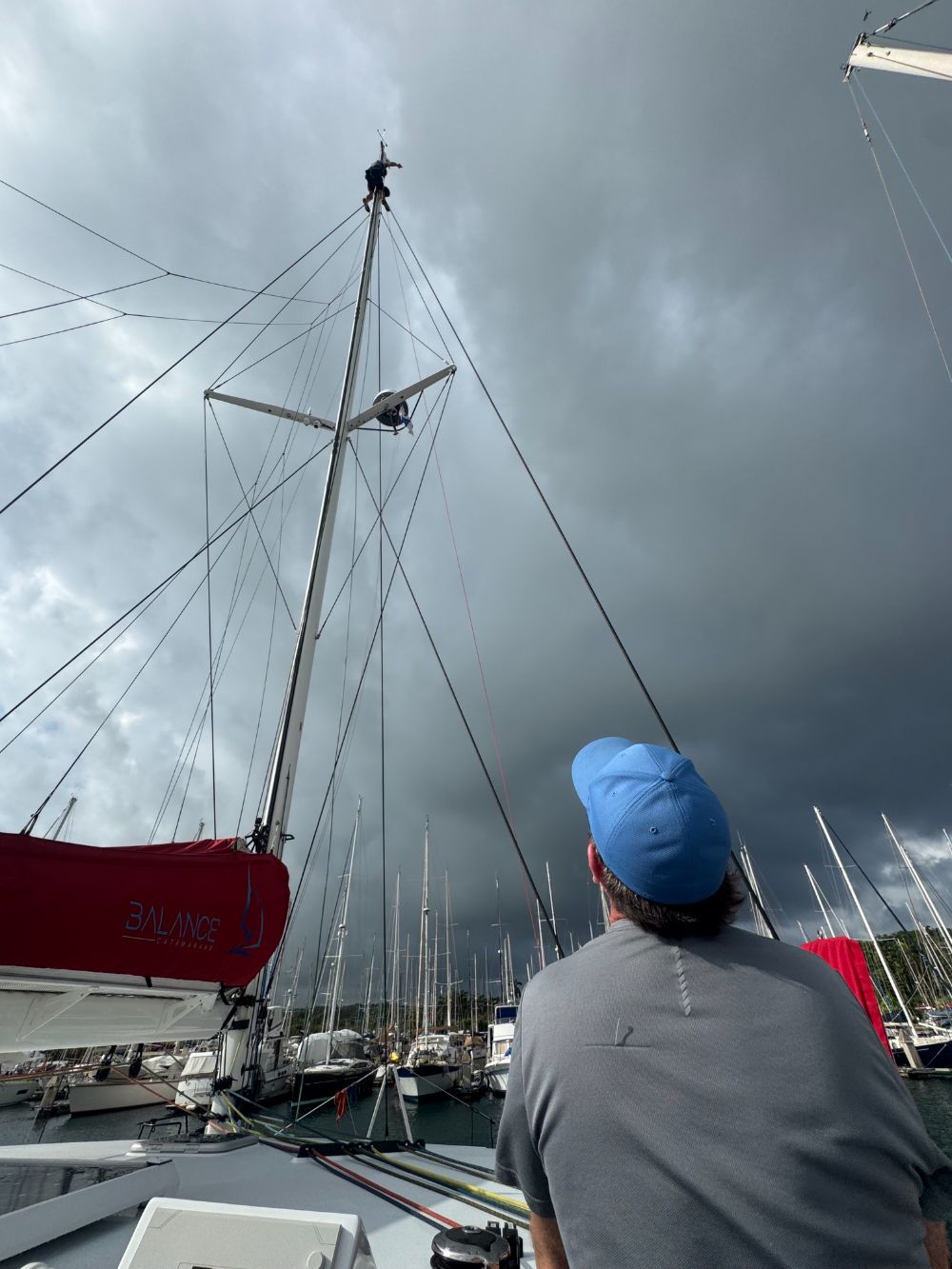 Rigger working at the masthead of a Balance catamaran while a crew member watches from the deck