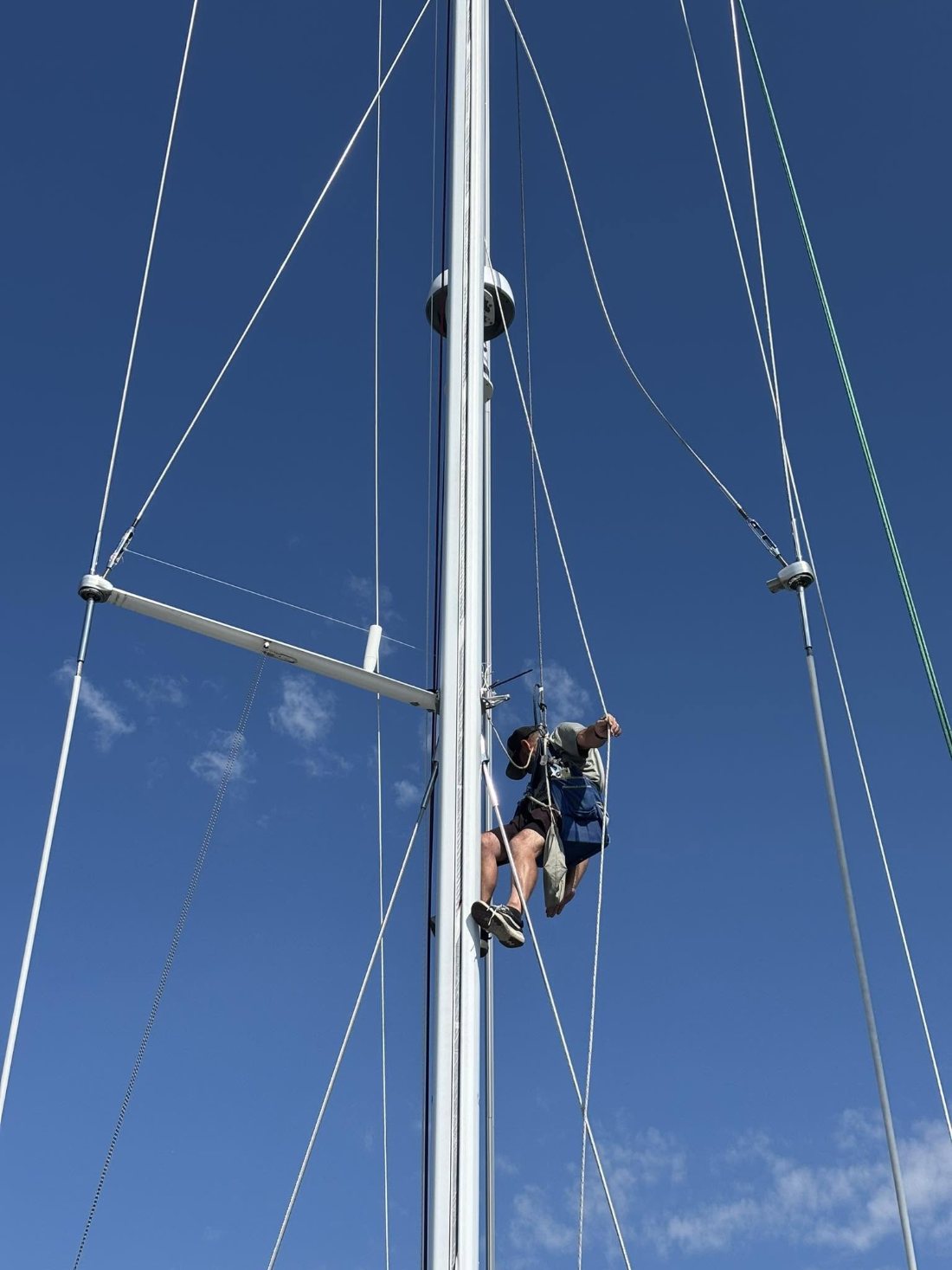 Rigger aloft in a bosun&rsquo;s chair inspecting a mast and spreaders